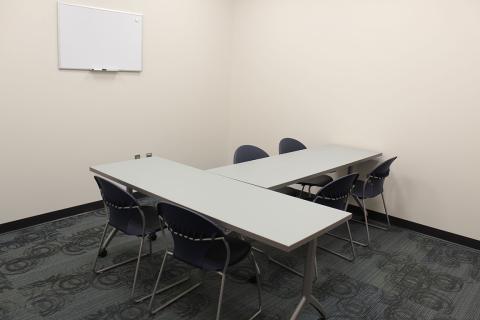 Room H with tables and chair. Dry Erase Board hanging on wall. 