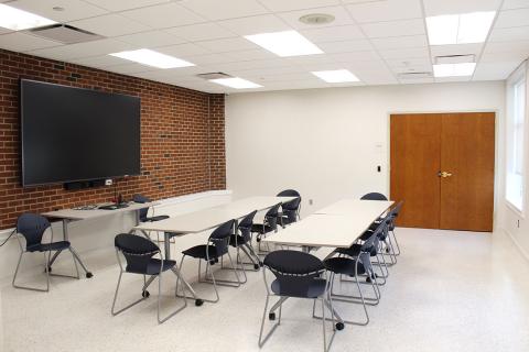 Room J with tables and chairs. A screen for showing presentations is installed on the wall. 